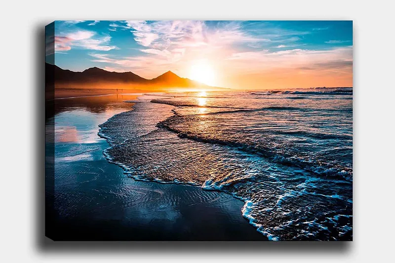Lerretsbilde 70x100 cm - Solnedgang over en strand med milde bølger som ruller inn mot kysten - Blå / Oransje / Turkis - Innredning - Bilder & kunst - Lerretsbilder